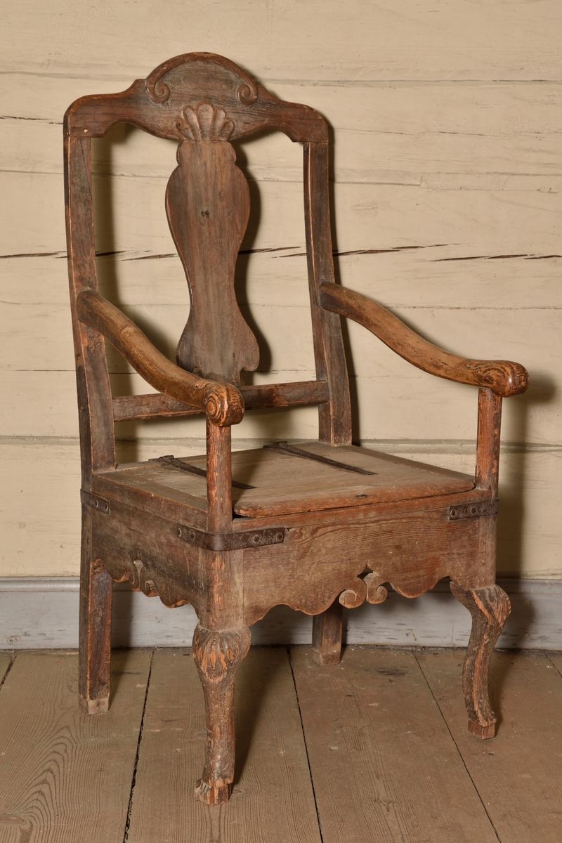 Stol tillverkad i björk och furu, rokokostil. Rak, delvis genombruten rygg med balusterformad ryggbricka. Krönet av stolsryggen med skuren ornering i form av voluter och snäcka. Lätt svängda armlän med dekorativt skurna avslut i form av voluter och akantusblad. Rak ostoppad sits i två delar, överst lucka med järnbeslag vilken går att fälla upp, under en sits med utskuret hål för placering av nattkärl. Bred sarg med skuren dekor i böljande vågmönster, samt var sida med genombrutet stjärnformat hål. Stolen vilar på fyra ben, de bakre enkla och raka, och de främre lätt svängda med skuren mussla.