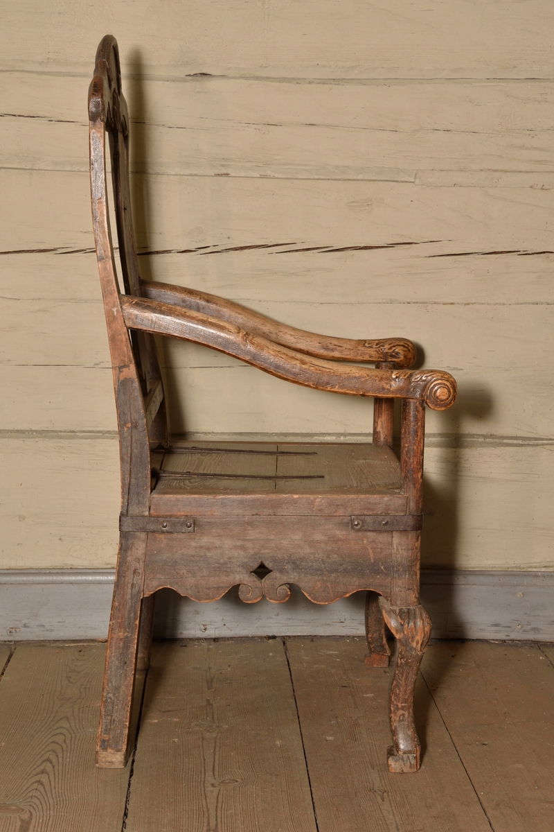 Stol tillverkad i björk och furu, rokokostil. Rak, delvis genombruten rygg med balusterformad ryggbricka. Krönet av stolsryggen med skuren ornering i form av voluter och snäcka. Lätt svängda armlän med dekorativt skurna avslut i form av voluter och akantusblad. Rak ostoppad sits i två delar, överst lucka med järnbeslag vilken går att fälla upp, under en sits med utskuret hål för placering av nattkärl. Bred sarg med skuren dekor i böljande vågmönster, samt var sida med genombrutet stjärnformat hål. Stolen vilar på fyra ben, de bakre enkla och raka, och de främre lätt svängda med skuren mussla.