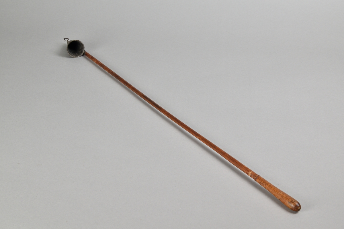 Ljussläckare av järnbläck med långt skaft i trä. Trattformad ljussläckare med järnkrok. Skaft med rundat avslut. 