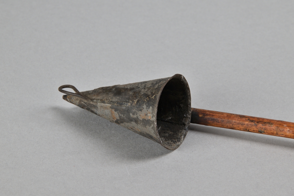 Ljussläckare av järnbläck med långt skaft i trä. Trattformad ljussläckare med järnkrok. Skaft med rundat avslut. 