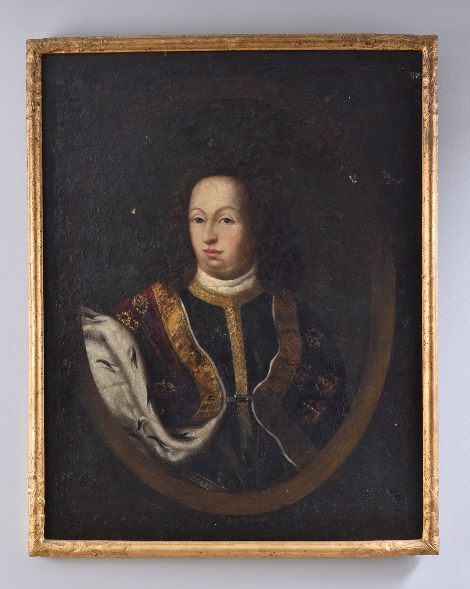 Porträtt föreställande Karl XI. Bröstbild. Karl XI med mörkt hår, klädd i mörk dräkt med vit krage och bräm i guld. Över dräkten en röd mantel med kant och detaljer i guld, samt fodrad med hermelin. Mörk bakgrund med oval ram.