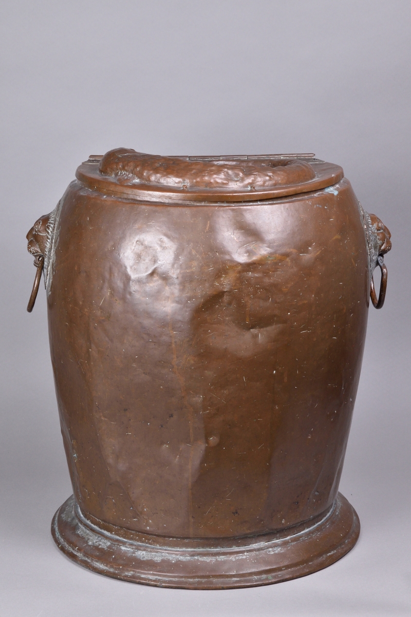 Kärl tillverkad av koppar. Hög och bred, med bukig överdel och avsmalnande underdel. Rakt avslut upptill med fällock på gångjärn, ornerat med driven dekor i form av fisk. Två handtag på var sida om kärlet, utformade som lejonhuvuden med ring. Kärlet vilar på en bred fotring.