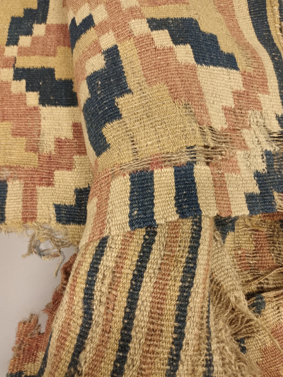 Ruteåkle i smett med enkle slyng over fire tråder.Truleg heimspunne og heimefarga garn både i renning og innslag. To tråds ullgarn, relativt hardt spunne. Fire åttebladsroser, ruteborder og striper nederst. Smal fald i begge korsidene. Teppet er særs slitt og falma.