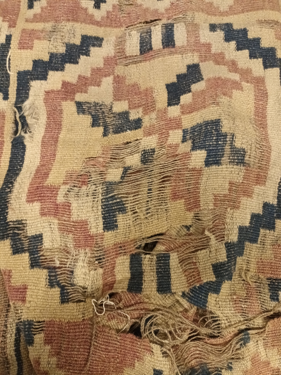 Ruteåkle i smett med enkle slyng over fire tråder.Truleg heimspunne og heimefarga garn både i renning og innslag. To tråds ullgarn, relativt hardt spunne. Fire åttebladsroser, ruteborder og striper nederst. Smal fald i begge korsidene. Teppet er særs slitt og falma.