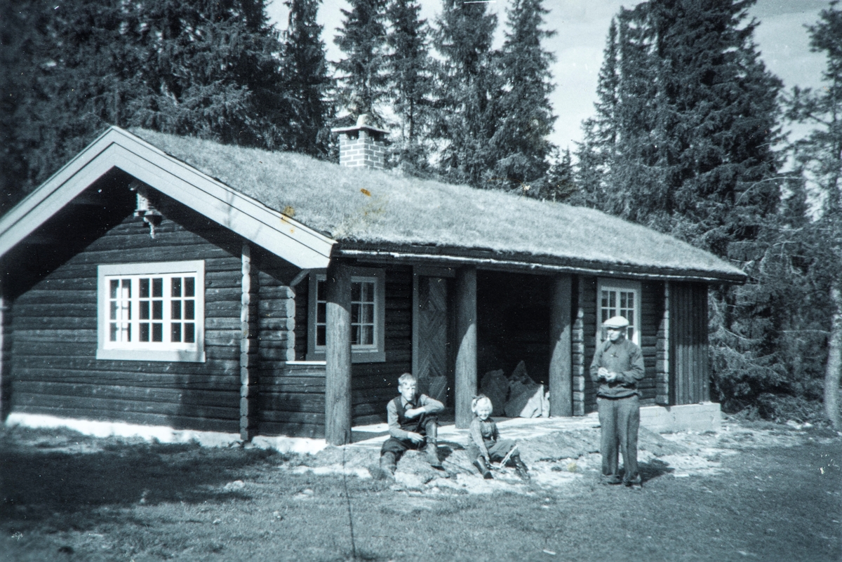 Skramstad (118/1). Skramstadhytta på Øya. Peder Husom til høgre. Kristen Prestrud og Ragnhild Prestrud på trappa. Skramstadhytta blant ned i 1944 etter tysk raid mot motstandsmenn, der to menn ble skutt. Denne hytta er gjenoppbygd etter krigen. Bildet er fra ca. 1952 og hytta er helt ny.