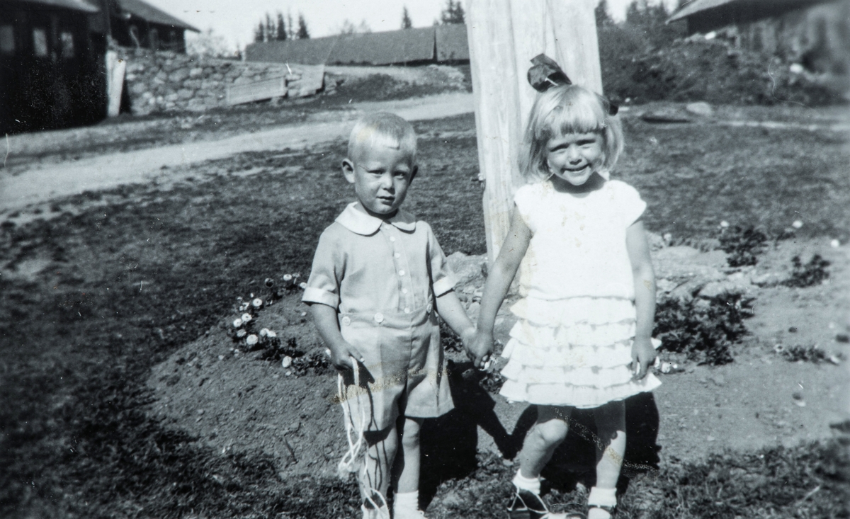Øvre Tomter (60/1). Helge Andreas og Helga Prestrud ved flaggstanga på Øvre Tomter. Bak låvebrua skimtes den gamle trøskelåven og til høgre gammelfjøset.  Trøskelåven måtte vike plassen for nyfjøset etter krigen.