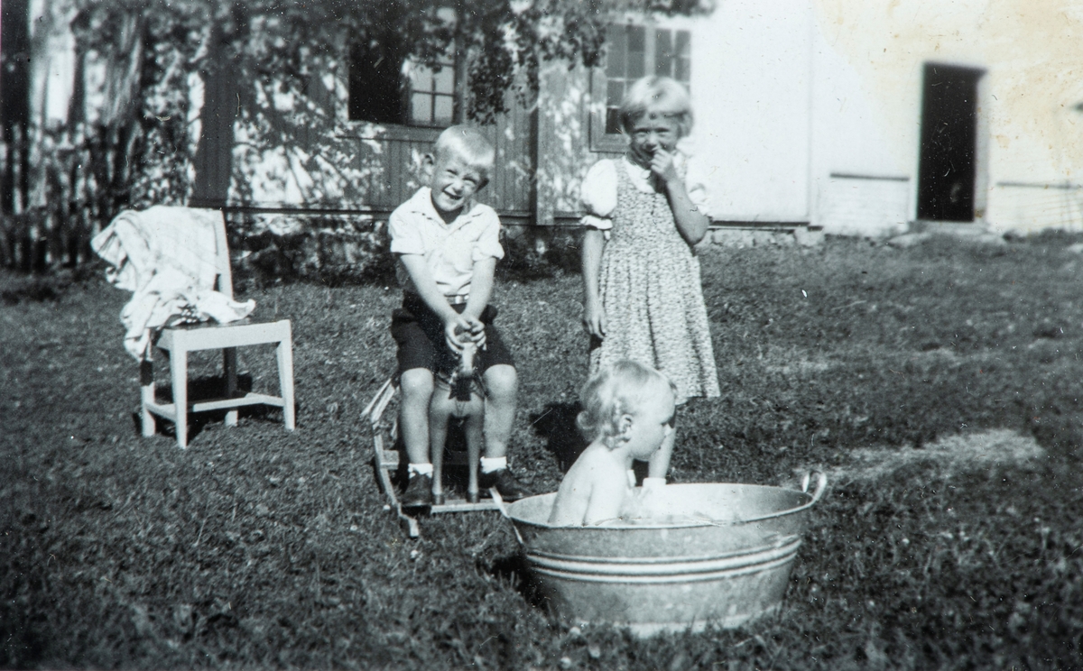Øvre Tomter (60/1). 1947. Helge Andreas sittende på en gyngehst, Helga og Ragnhild i hagen på Øvre Tomter. Yngstejenta Ragnhild sitter i badebalja. Sinkbalje.