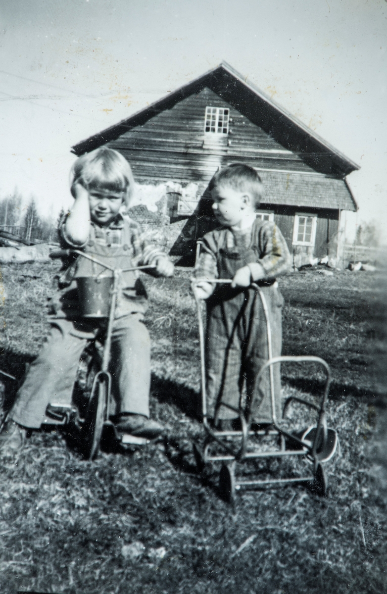 Øvre Tomter (60/1). Helga og Helge Andreas Prestrud ute å leker i hagen, trehjulsykkel og restene av en barnevogn. ca. 1934. Bak ser vi steinfjøset med laftet overbygg. Et lite hønsehus er bygd på til høyre.