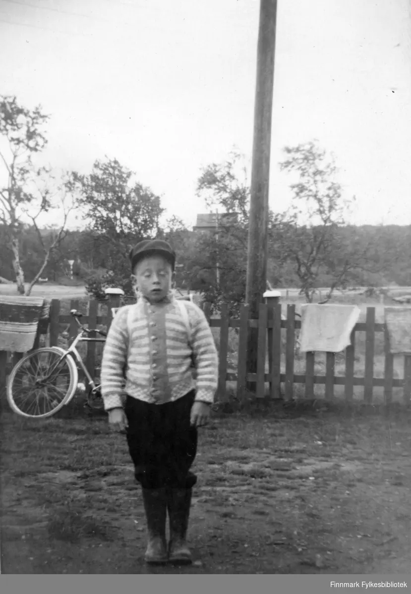 Arnfinn Moens første skoledag i 1960. Bildet er tatt utenfor huset/bakeriet, og i bakgrunnen sees vegkrysset og lærerboligen i Varangerbotn. Tepper luftes, de er lagt over gjerdet.