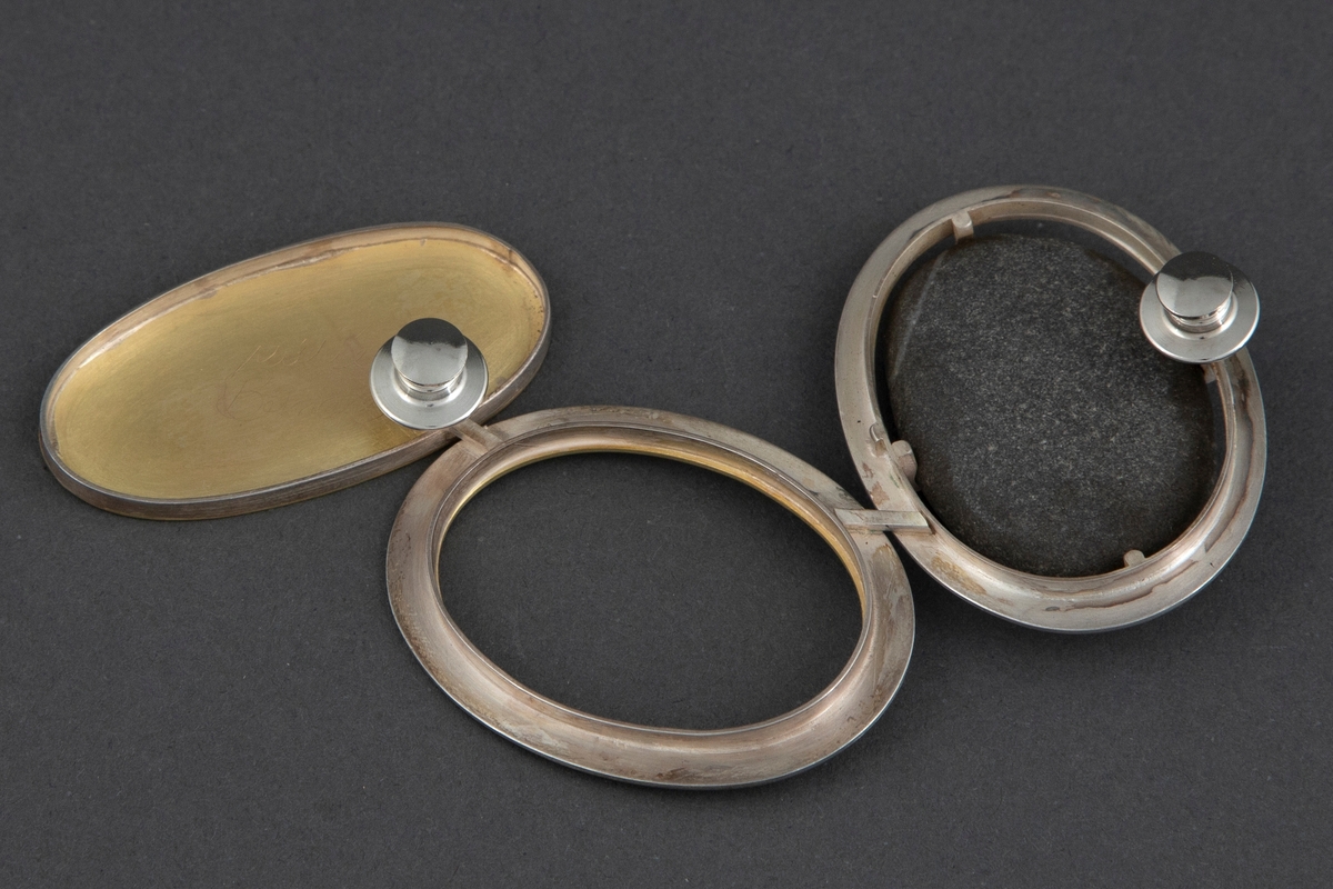 Brosjen er satt sammen av tre ovale ringer i børstet sølv og gull. Sølvringen holder på en svart rullestein. Åpen ring i midten av sølv med en liten gullkant i veggene. Ringen til høyre har en heldekkende gullplate med sølvvegg. De tre ringene er festet sammen på baksiden med sølvstaver. Brosjen har to pinfester. På baksiden av gullplaten er det inskribert signaturen Millie Behrens.