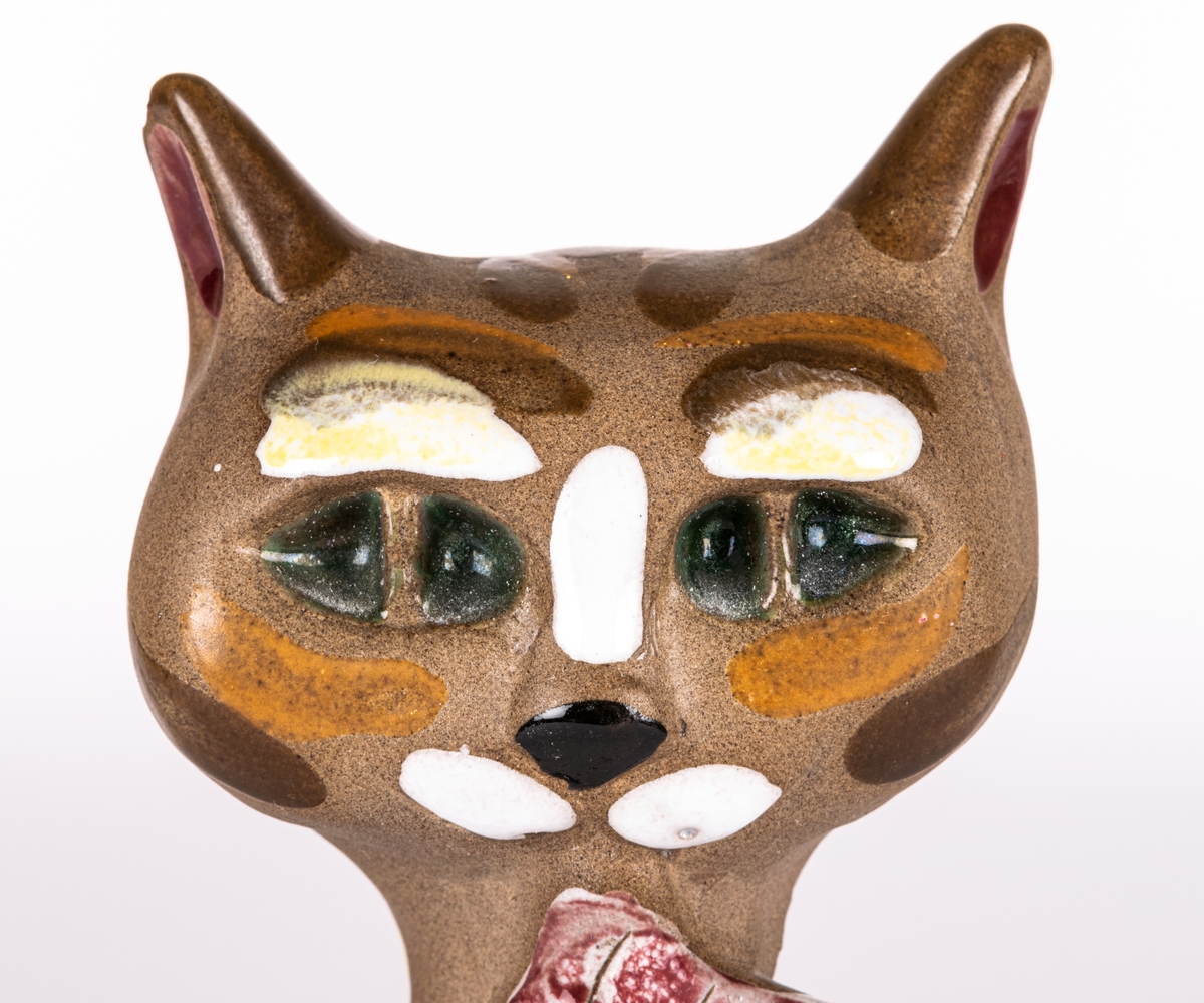 Figurin i form av katt med en liten fisk i munnen,  brunfärgat lergods med glaserade detaljer. Formgiven av Dorothy Clough för Gefle Porslin 1955.