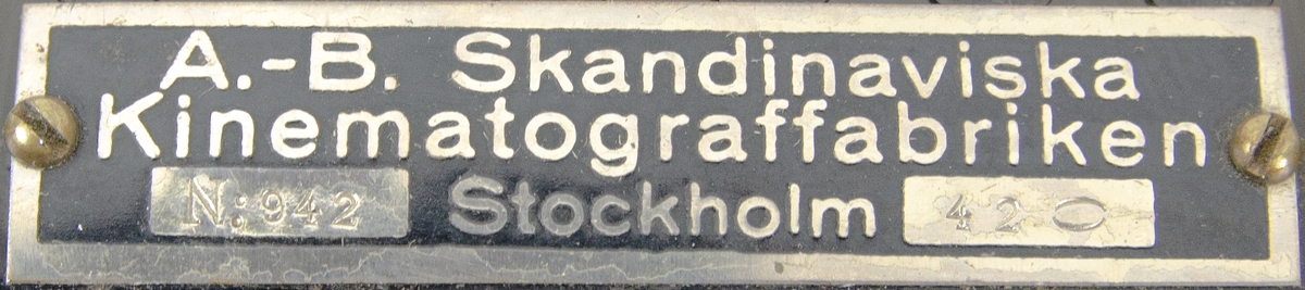 Filmprojektor 16 mm, Pathe Rural, med tillbehör. Bland annat en transformator. Förvarad i en specialanpassad trälåda som stängs med en metallpinne. Lådan är märkt med "5001" och "RURAL" på framsidan och "APPAREIL DE CINEMA" på baksidan.