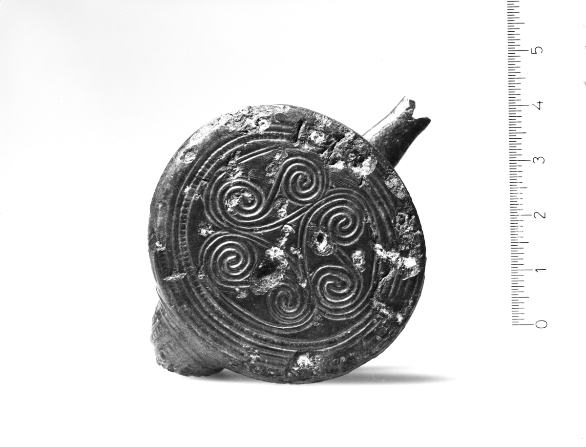 "Beltekrog" af Bronce fra Broncealderen, lig Müller, Broncealderen No. 37 og Montelius, En tidsbestämning pl. II, fig. 28. Den afviger fra begge disse ved at have en nedad fremskydende Spids bagtil i Fortsættelse af den bagret ret opad gaaende Stift. Den har Spiralfornamenter ganske i samme Stil som paa de anførte svenske og danske Exemplarer. Er den første i Norge fundne Beltekrog fra Broncealderen; lidt beskadiget oventil ved Affiling.