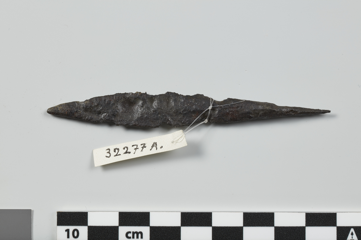 Pilespiss av jern av form som R. 539, men mindre enn typeeksemplaret, nærmest lik Kulturhistorisk leksikon XIII, s. 278, fig. c (tekst spalte 273). Se også Jan Petersen: Vikingesverd, s.48. Nåværende eksemplar er påfallende kort med opphøyd midtribbe, kort tange. Fortykket mellom tange og blad. Litt skadet i den ene egg. Lengde 9,2 cm, st.br. 1,3 cm.