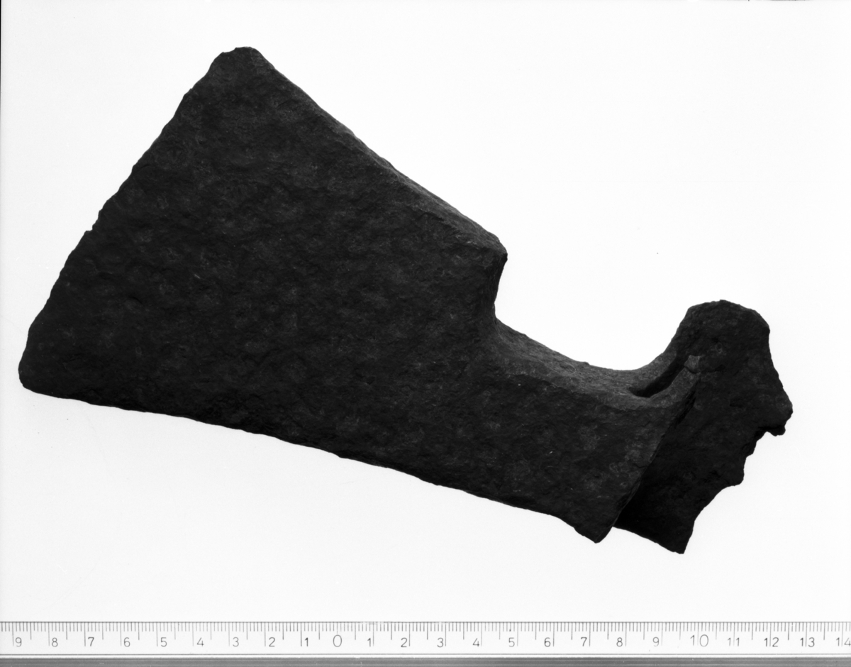 Økseblad av jern. Skjeggøks med innad skrånende rygg og skrått avskåret skjegg. Skaftholk med rundt skafthull og avrundete fliker. Skaftholken defekt. Lengde 19,8 cm, eggens br. 11 cm. 1200-1600-årene.