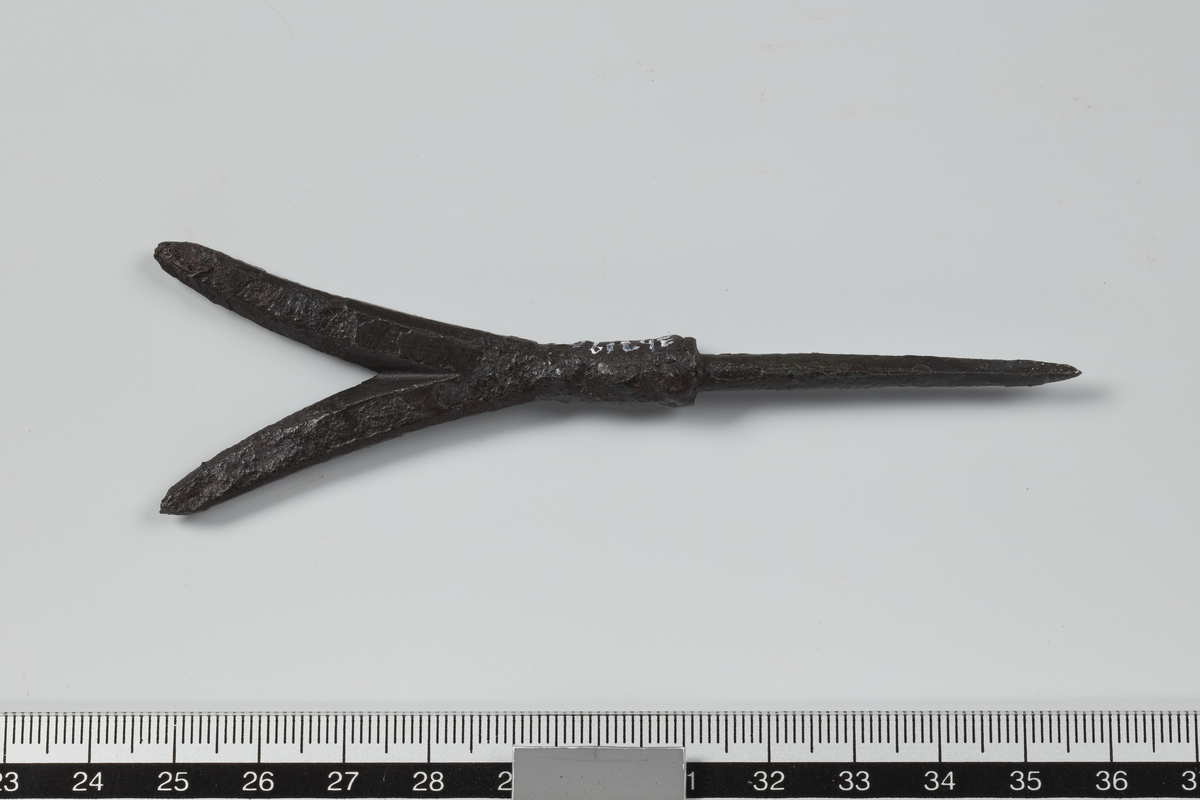 Pil av jern med tvedelt odd og markert overgang fra blad til tange. Velbevart. Stl. 10,9 cm, stb. 3,2 cm, tangens l. 4,5 cm.