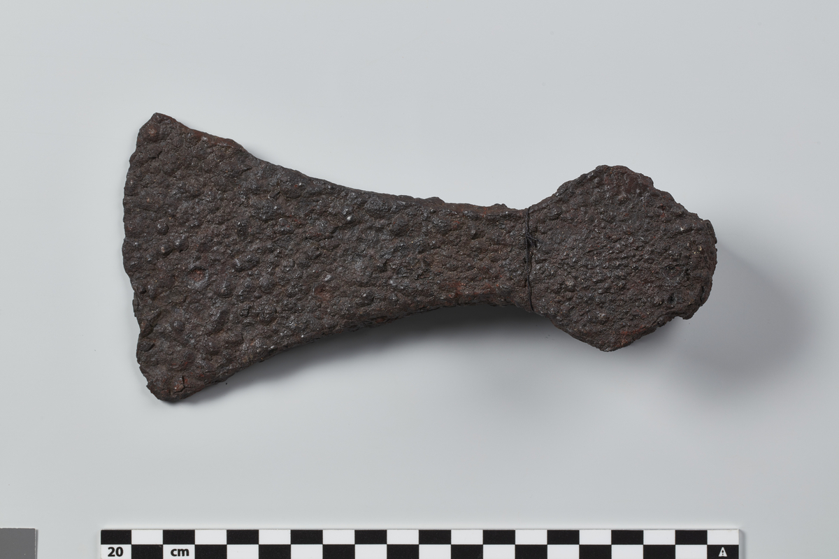 Øks av jern av form som Jan Petersen: De norske vikingesverd fig. 38, men med litt smalere eggparti og mindre markerte skaftfliker. Nokså forrustet, litt avslått ved skafthullpartiet og eggen. Lengde 18,7 cm. Bladets største bredde (over eggen) 9,1 cm.