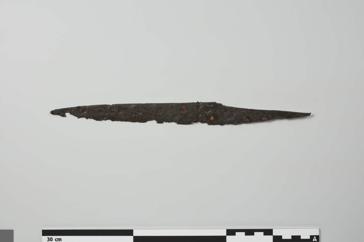 Jaktkniv av jern omtrent som Fett: Arms in Norway, fig. 64, med avsats mellom tange og blad på ryggsiden. Noe forrustet, men hel og godt bevart. Lengde 29 cm, st. bredde 3,7 cm.