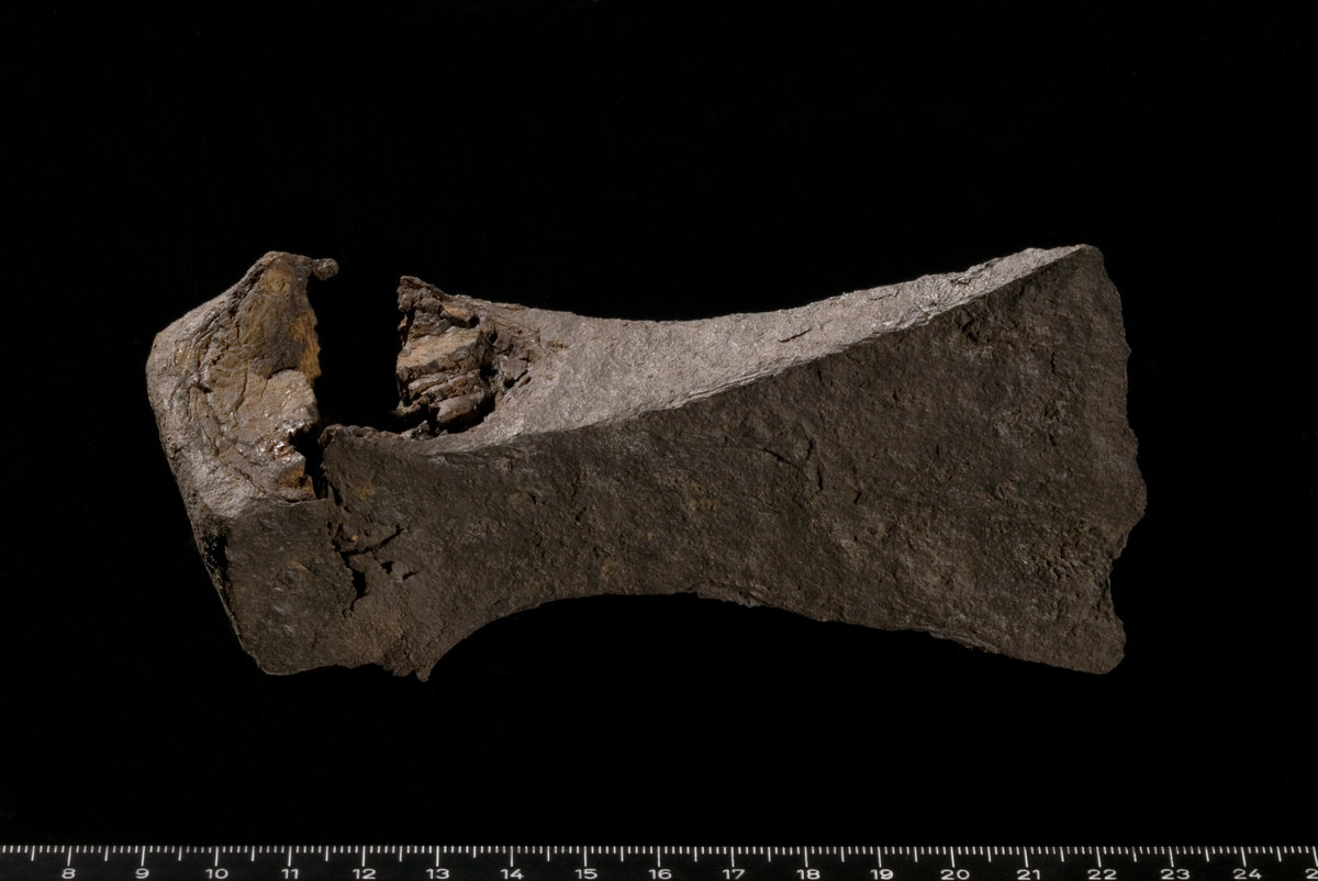 Øks av jern nærmest som Petersen Type G/fig. 38 (Petersen 1919). Skaftehullet er sprukket på en side, devis sprukket på den andre. Øksen er svært korrodert. Mulige rester av mineralisert tre i skaftehullet. 