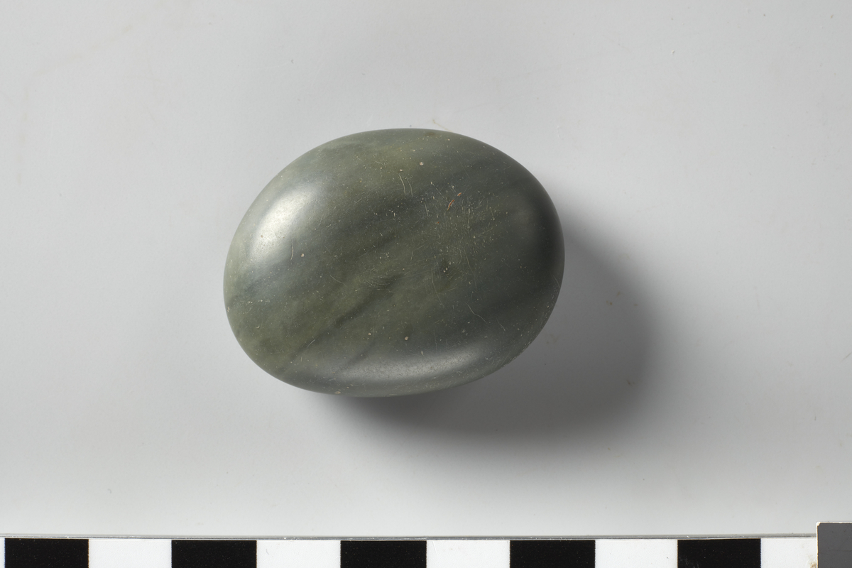 1 grågrønn, oval, glattestein. Blank, glatt overflate. Stl: 4 cm. Stb: 3 cm. Stt: 1,4 cm. 