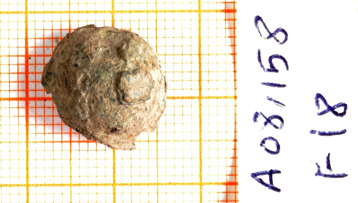 Liten, oval prydnagle eller prydbeslag av kobberlegering (1,53 x 1,37 cm). Liknende form som nr. 1. Både over- og undersiden er totalt korrodert og kun en liten del av av opprinnelig overflate er bevart. 
