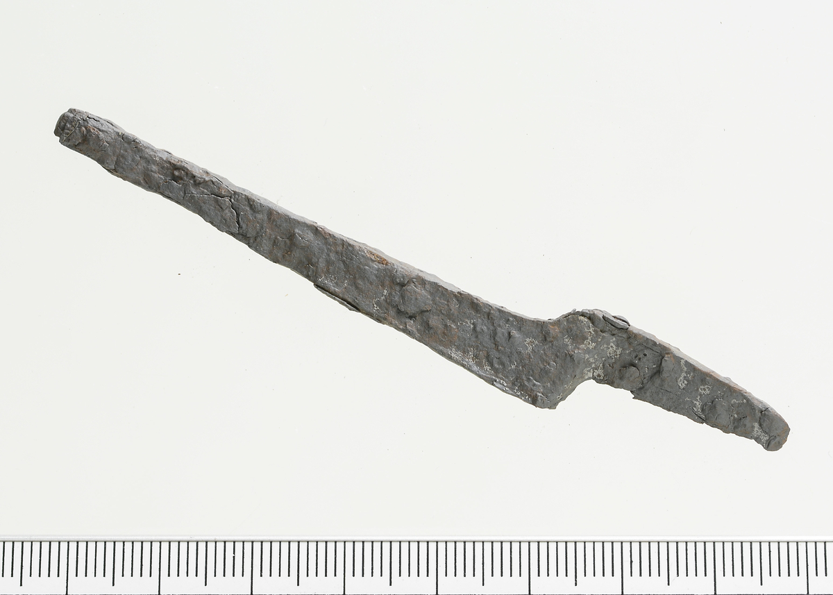 Krumkniv av jern uten klare paralleller. Mål: Stl: 9,1 cm. Stb: 1,5 cm. Stt: 0,3 cm. Tangens. l.: 3,7 cm. Vekt: 8,6 g.