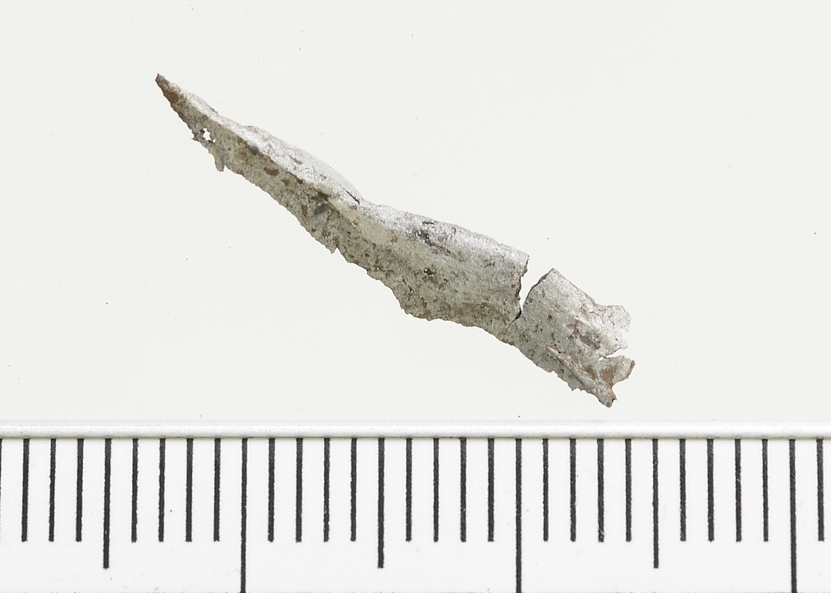 Fragment av en nål av jern med firkantet tverrsnitt og brudd i en ende. Mål: Stl: 2,1 cm. Stb: 0,3 cm. Stt: 0,2 cm. Vekt: 0,2 g.