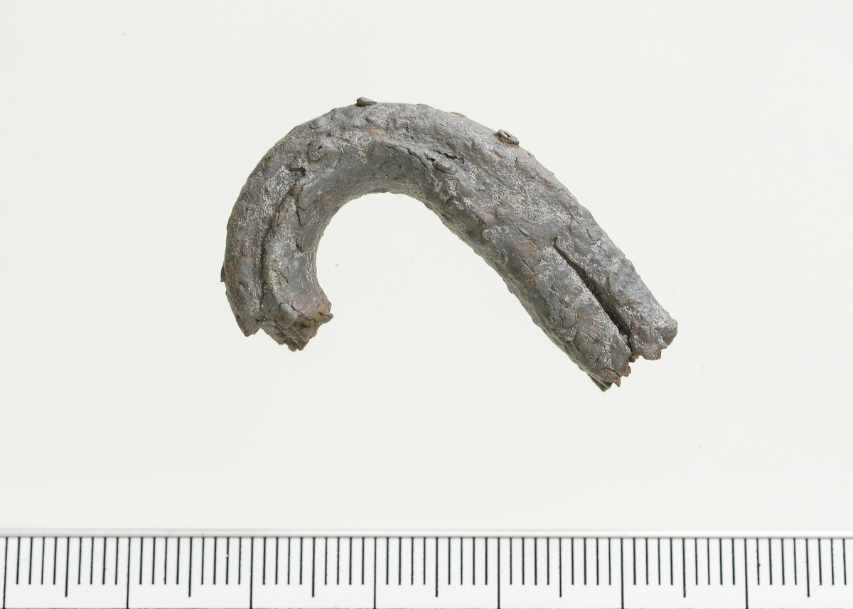 Fragment av en lenke til kjetting eller krok av jern med firkantet tverrsnitt. Mål: Stl: 3,7 cm. Stb: 2,7 cm. Stt: 1,0 cm. Vekt: 19,3 g.