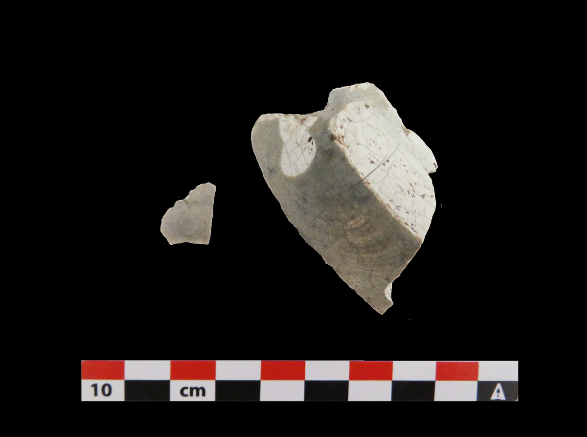 Fragment av flint. Fragmentet er hvitbrent, og stykkets største side er dekket av cortex. 2,2 cm av en sidekant har spor etter bearbeiding eller bruk som ildflint.