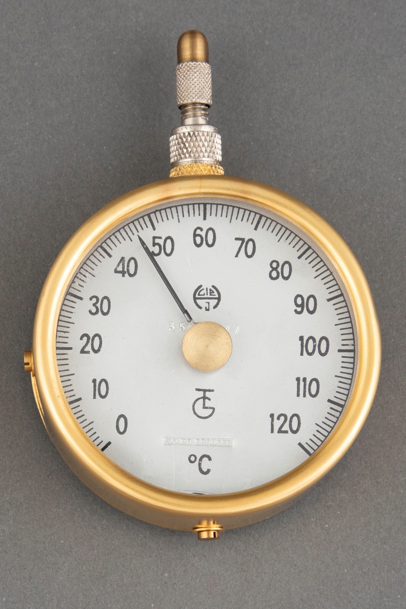 Brosjen er satt sammen av en formessinget temperaturmåler og en sykkelventil i aluminium. Tallskiven viser fra 0 - 120 °C. Kunstnerens signatur er påført tallskiven i form av et stempel. Brosjens bakside har en messingplate med en nål og er skrudd fast til hovedformen med to skruer på siden og en skrue på undersiden.