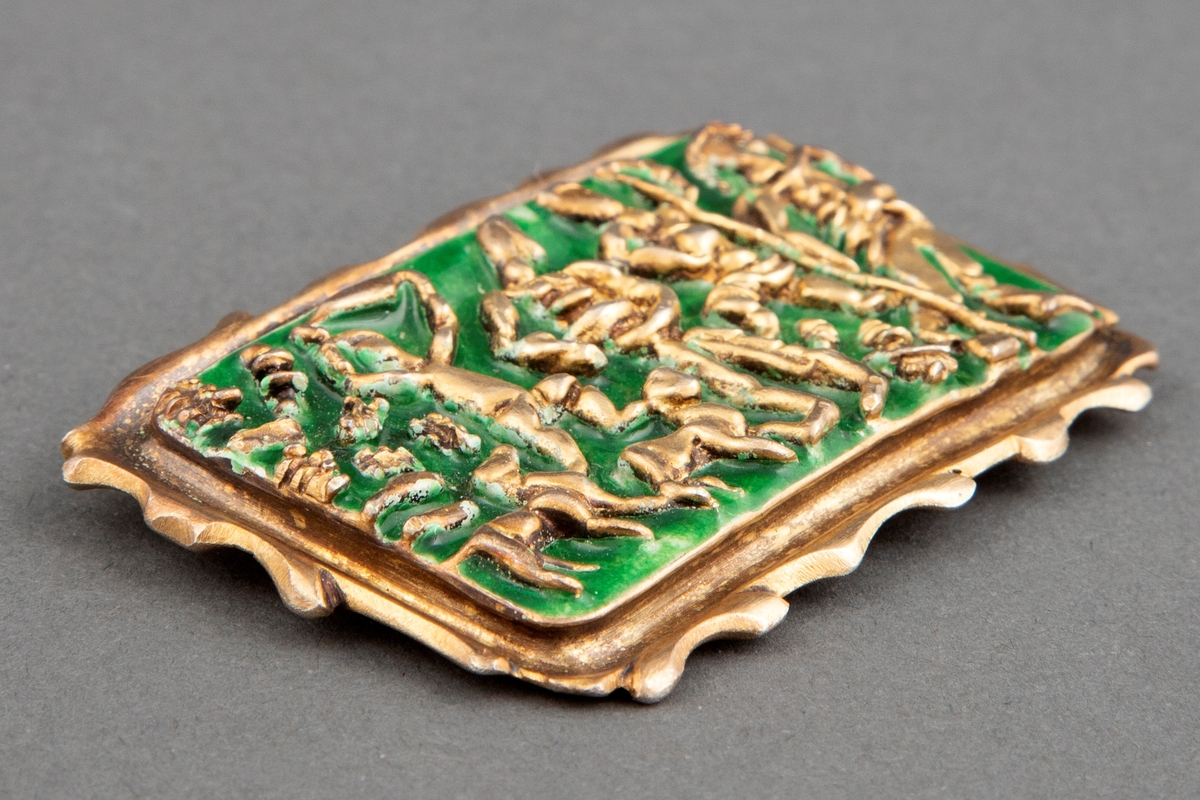 Rektangulær brosje i forgylt sølv med grønn emalje. Pastoralt motiv med fire stiliserte menneskefigurer og to dyr.