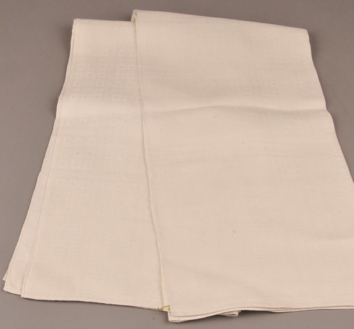 Duk av lin. Einsfarga med rutemønster. Relativt blank på rettsida. Falda med små faldesting for hand i begge kortsidene.