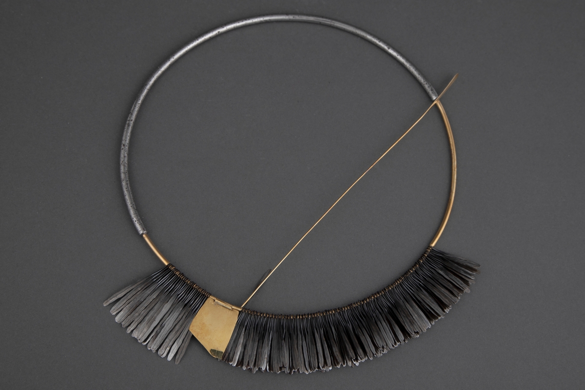 Halsklave bygget opp som en sirkel med en halvdel i gull og en halvdel i stål som er felt i hverandre. På 2/3 deler av gulldelen er det festet en krans av smidde spikre. Disse er kokt i linolje og har fått en mørk grå-svart farge. Litt nedenfor toppen av denne kransen er det festet en gullplate med skravert mønster. Fra denne løper en gullstav over og ned til den andre siden. Ved bruk løper denne foran halsen.