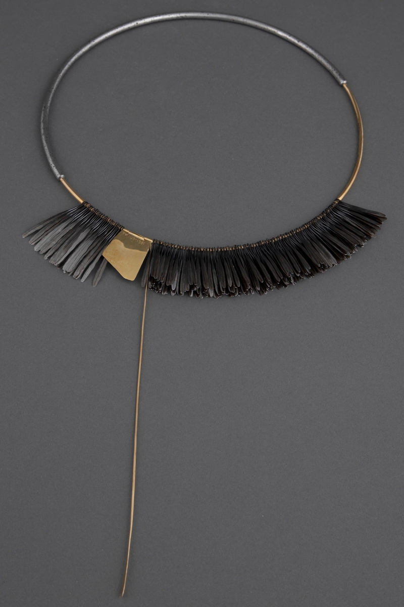 Halsklave bygget opp som en sirkel med en halvdel i gull og en halvdel i stål som er felt i hverandre. På 2/3 deler av gulldelen er det festet en krans av smidde spikre. Disse er kokt i linolje og har fått en mørk grå-svart farge. Litt nedenfor toppen av denne kransen er det festet en gullplate med skravert mønster. Fra denne løper en gullstav over og ned til den andre siden. Ved bruk løper denne foran halsen.