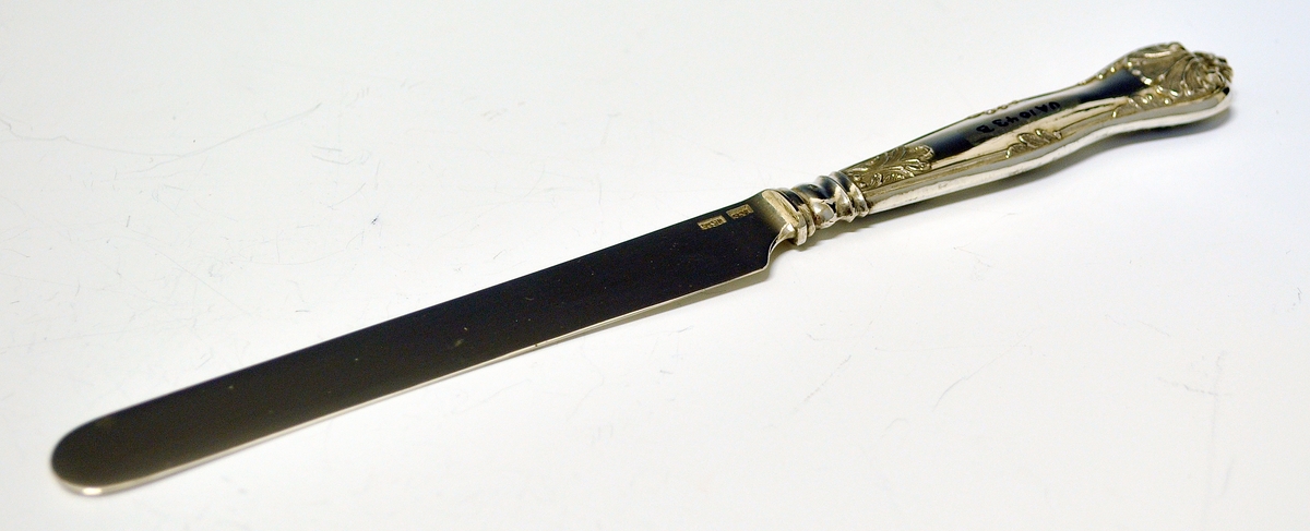 Kniv med skaft. Tilhører antakeligvis bestikksett med skje og gaffel. Bordkniv med butt knivblad. Skaftet har dekorert relieff i muslingmønster og qravert inn: C.C.C.A. 1835.(Christine Cecilie Charlotte Aall).