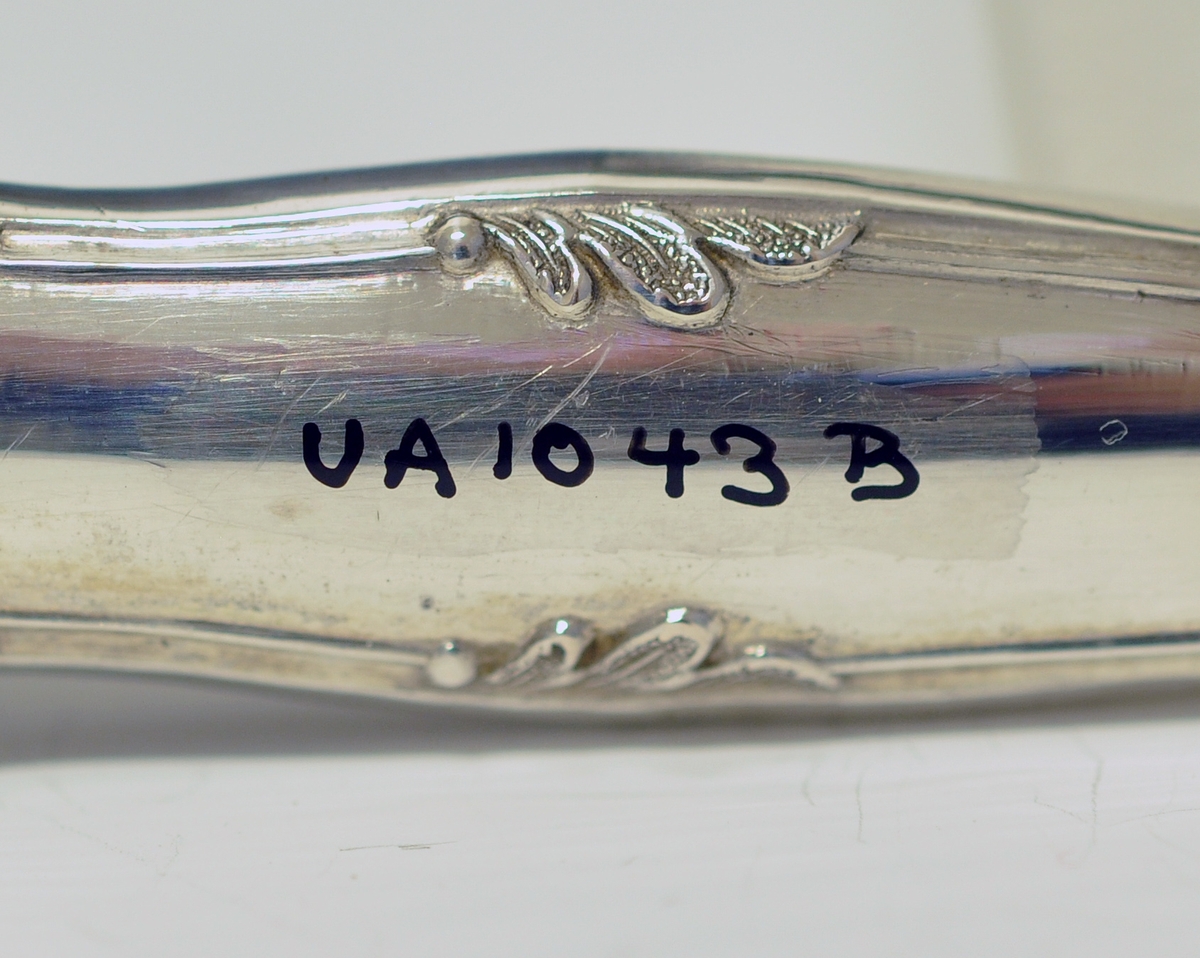 Kniv med skaft. Tilhører antakeligvis bestikksett med skje og gaffel. Bordkniv med butt knivblad. Skaftet har dekorert relieff i muslingmønster og qravert inn: C.C.C.A. 1835.(Christine Cecilie Charlotte Aall).