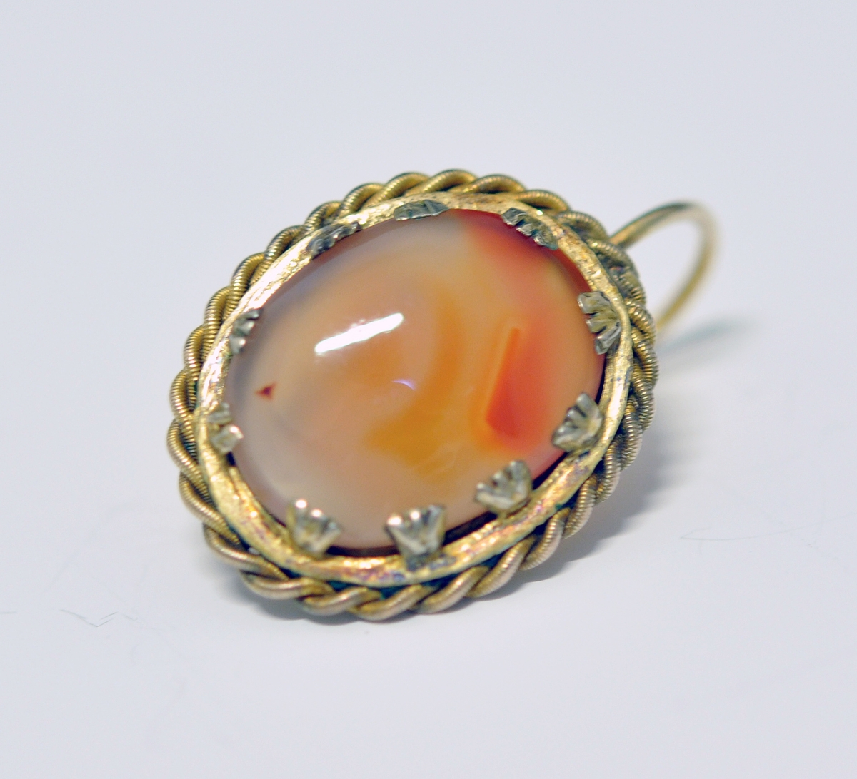 Smykkesett som består av 1 stk brosje, og 2 stk øreheng. A.Oval nesten kvadratisk brosje som består av  brun-orange stein (agatl?). Steinen er omkranset av smal metallkant  som er snodd rundt steinen, og  festet med små "blad" Steinen vises også på baksiden, og en smal nål er montert på.

B. og C. Øreheng/pynt i samme utførelse som brosjen, det er montert en lang bøyle til feste.  

D. Brunrød smykkeeske medfølger, på baksiden kan det være et stempel eller nr?