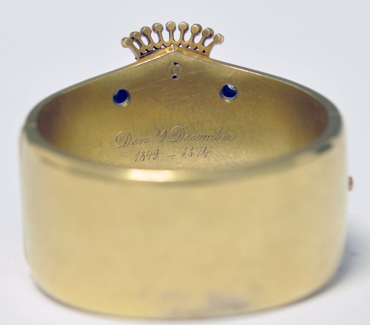 A.Bredt gullarmbånd som kan åpnes  på siden med lås og sikkerhetslenke. Armbåndet går i en spiss foran og det er montert en krone øverst men flere små diamanter, kronen er noe løs. Foran har armbåndet tre lokk  som kan åpnes. Framsiden av lokkene er dekoret med initialer i diamanter :  NWJ. Hvert lokk kan åpnes og inneholder fire fotografier av mannspersoner.Innvendig er det gravert inn årstall og stemplet.

B. Lilla eske smykkeeske som er tilpasset armbåndets form og har lås. Innvendig i lokket er firmaets navn stemplet.