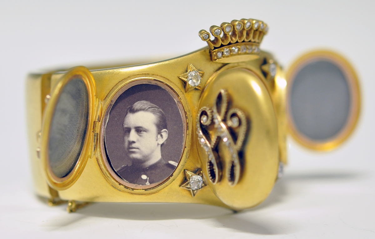 A.Bredt gullarmbånd som kan åpnes  på siden med lås og sikkerhetslenke. Armbåndet går i en spiss foran og det er montert en krone øverst men flere små diamanter, kronen er noe løs. Foran har armbåndet tre lokk  som kan åpnes. Framsiden av lokkene er dekoret med initialer i diamanter :  NWJ. Hvert lokk kan åpnes og inneholder fire fotografier av mannspersoner.Innvendig er det gravert inn årstall og stemplet.

B. Lilla eske smykkeeske som er tilpasset armbåndets form og har lås. Innvendig i lokket er firmaets navn stemplet.