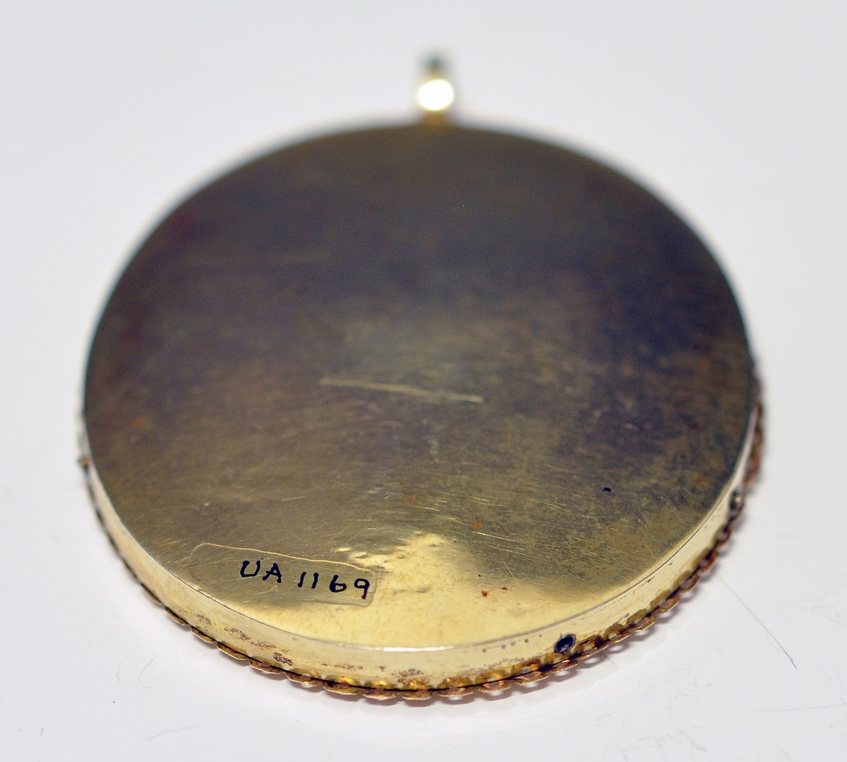 A..Ovalt miniatyrportrett av mann  i midten. Portrettet er innrammet av en smal bølget
perforert krans ytterst i metall og dekket med glass. Øverst oppe er det montert en ring for kjede. Kjedet mangler. Baksiden består av metall. 

B. Oval rød smykkeeske i skinn utvendig og tekstil innvendig.  Har lås og fast lokk som kan åpnes. Ingen stempel.