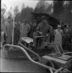 Skogsdag Örserums brunn 1961. I mitten på bilden står en plog som drivs av ett fordon. Plogen har en sits och en man i arbetskläder håller precis på att slänga benet över plogen för att sätta sig. Flera män står bredvid och titta.