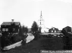 Lidens kyrka. Till vänster troligen gamla sockenstugan. Vägen går ned till Lidens Färjeläge