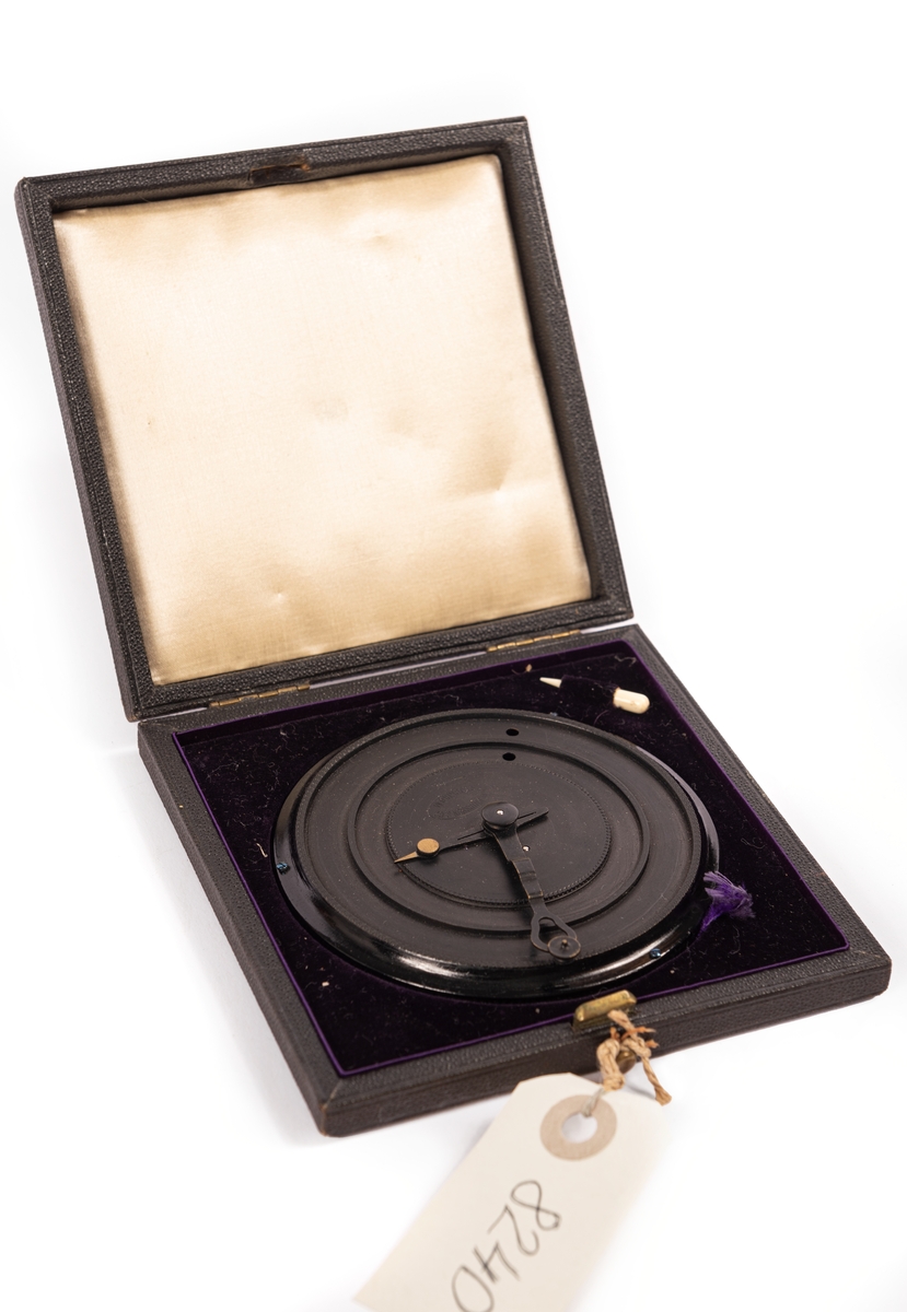 Kryptograph för Kungliga flottan, 1887 års modell.

Svartlackerad rund plåtskiva, vilande på tre små skruvar. Skivan med två nedfällda ringplan, vardera med ett hål, samt två centrumvisare, den mindre med omålad spets. Märkt: ”LM Ericsson & Co Stockholm". Tillhörande läderklätt svart fodral, invändigt fodrat med violett sammet och i locket med vitt siden. Infälld en liten elfenbenspryl. Knäpplås.