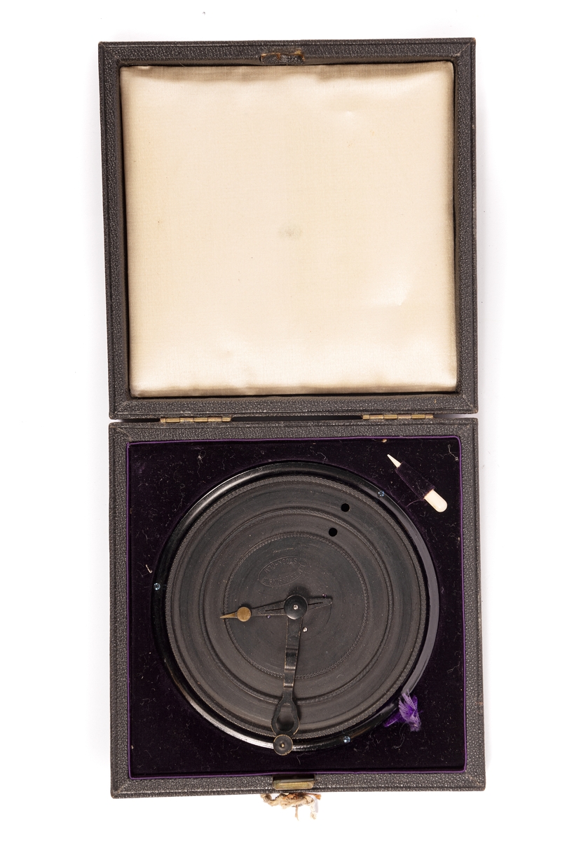 Kryptograph för Kungliga flottan, 1887 års modell.

Svartlackerad rund plåtskiva, vilande på tre små skruvar. Skivan med två nedfällda ringplan, vardera med ett hål, samt två centrumvisare, den mindre med omålad spets. Märkt: ”LM Ericsson & Co Stockholm". Tillhörande läderklätt svart fodral, invändigt fodrat med violett sammet och i locket med vitt siden. Infälld en liten elfenbenspryl. Knäpplås.