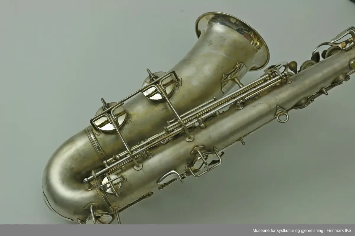 En altsaksofon med kasse produsert i Tyskland av H.G. Hüller. Laget av messing og med enkelt rørblad. Saksofonen har gravert dekor med logo av fabrikkprodusent "G.H.Hüller Saxophonefabrick Schöneck i.V". Saksofonen består av munnstykket, hals og kropp. Den har 24 klaffer med 9 knapper av perlemor. Klaffene er på innsiden dekket av et hvit kunststoff. Nummeret "43311 L" er gravert på baksiden rett ovenfor buen.