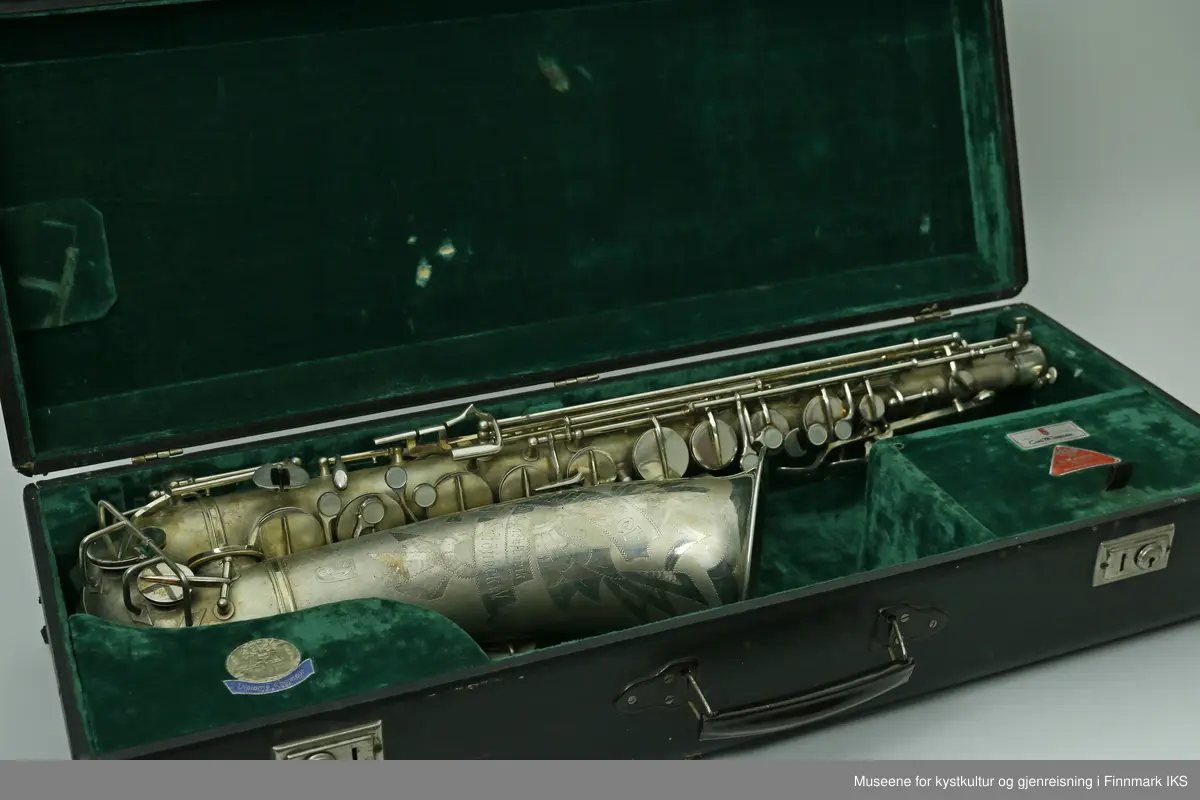 En altsaksofon med kasse produsert i Tyskland av H.G. Hüller. Laget av messing og med enkelt rørblad. Saksofonen har gravert dekor med logo av fabrikkprodusent "G.H.Hüller Saxophonefabrick Schöneck i.V". Saksofonen består av munnstykket, hals og kropp. Den har 24 klaffer med 9 knapper av perlemor. Klaffene er på innsiden dekket av et hvit kunststoff. Nummeret "43311 L" er gravert på baksiden rett ovenfor buen.