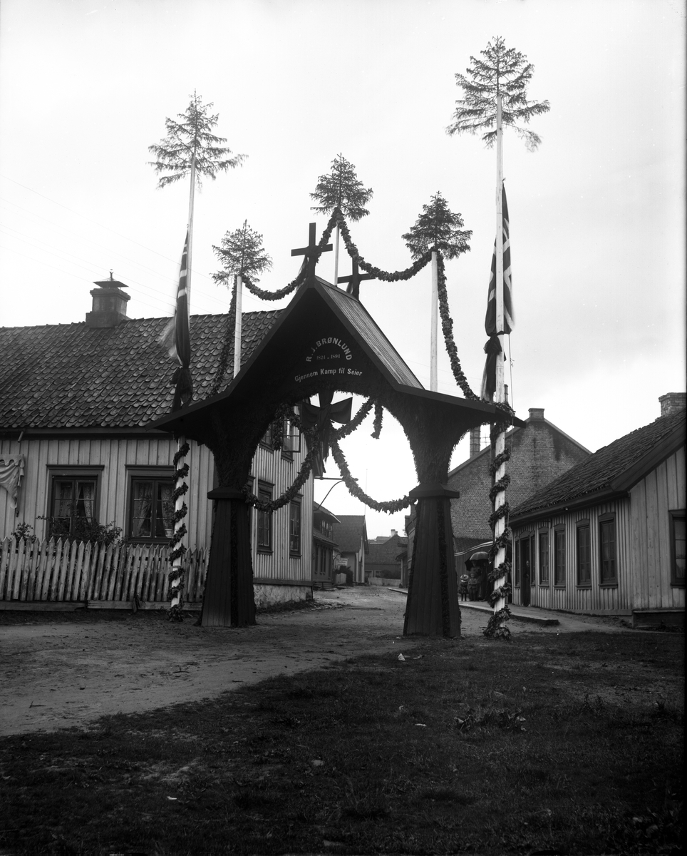 Fotosamling etter fotograf John Nielsen, Porsgrunn. Motiv med æresportal i forbindels med Rasmus Jørgensen Brønlunds (1824-1894) begravelse. Brønlund var grunnlegger av Porsgeund Mekaniske verksted og Skiensfjordens Skole til utdanning af mekaniske arbeidere.