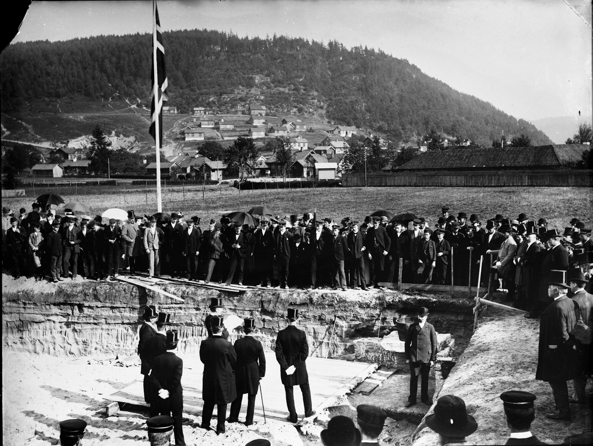 Fotosamling etter fotograf John Nielsen, Porsgrunn. Motid fra grunnstensnedleggelse ved Skiensfjorden Mekaniske Fagskole på Osebakken 22 september1894. Arkitekten var Haldor Larsen Børve og tomten var stillet til rådighet av Gunnar Knutsen. Byggingen var et spleiselag mellom offentlige og private aktører. Bygget var klar til inflytting 1895. Gunnar knudsen sees antakelig til høyre i fotografiet.