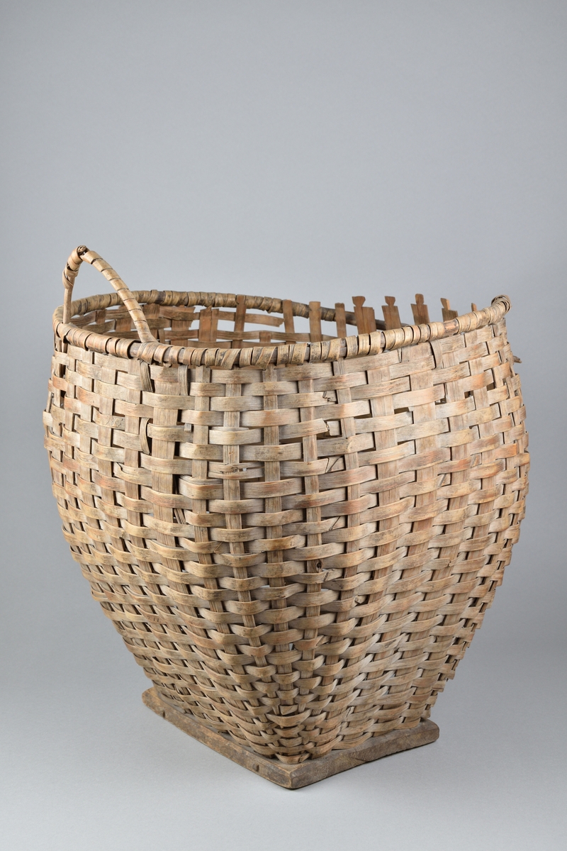 Ullkorg tillverkad av flätat träspån. Rund och bukig överdel, med bred öppning samt med ett handtag. Nederdelen avsmalnande. Korgen vilar på en rektangulär fotplatta av trä.
Korgen har möjligtvis haft ett ytterligare handtag vilket numera saknas. 