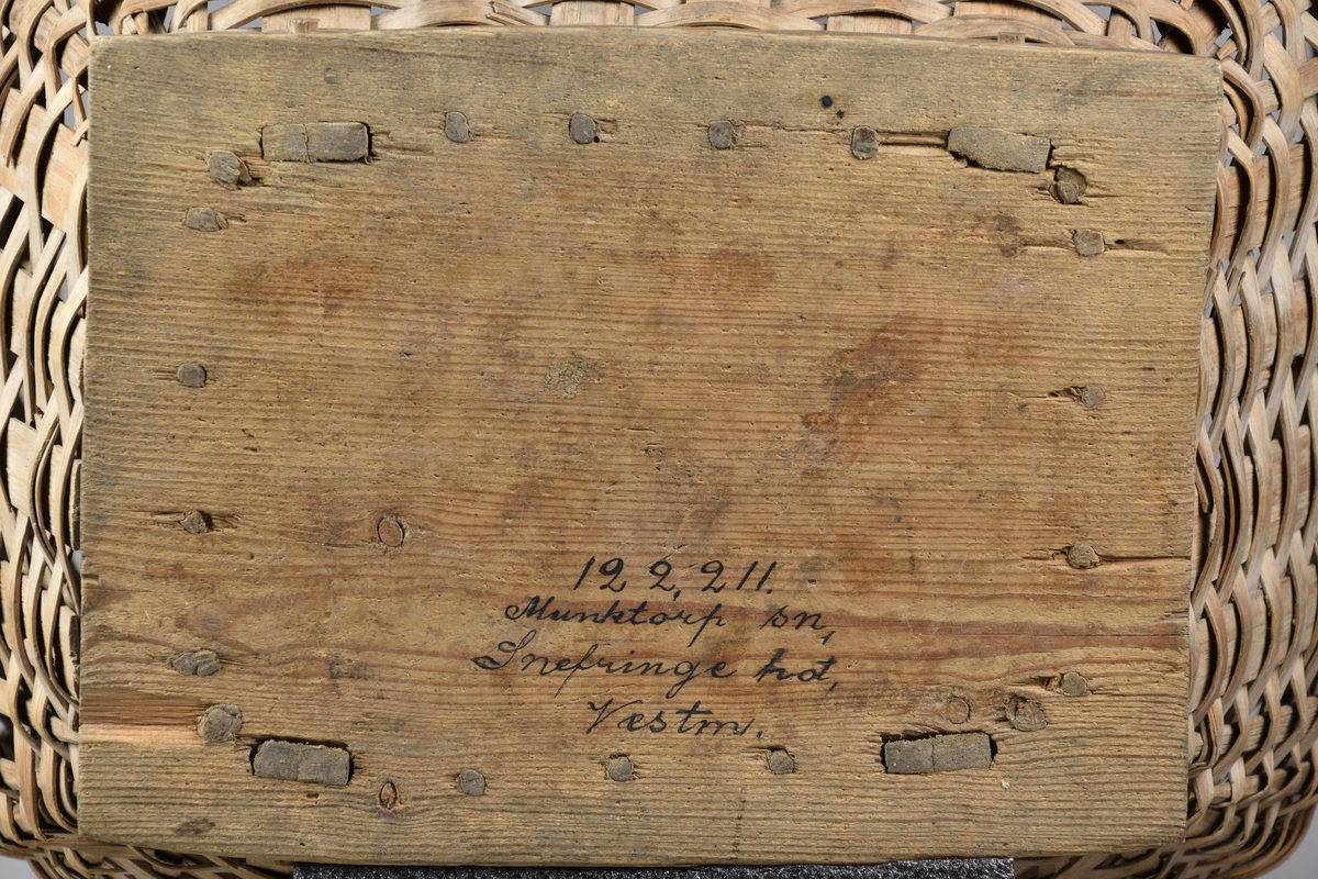 Ullkorg tillverkad av flätat träspån. Rund och bukig överdel, med bred öppning samt med ett handtag. Nederdelen avsmalnande. Korgen vilar på en rektangulär fotplatta av trä.
Korgen har möjligtvis haft ett ytterligare handtag vilket numera saknas. 